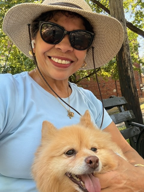Yamil Sarabia in a sun hat, smiling, holding Nyla, a fluffy Pomeranian